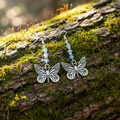 Butterfly dangle earrings with silver butterfly charms and light blue beads on a woodsy natural background