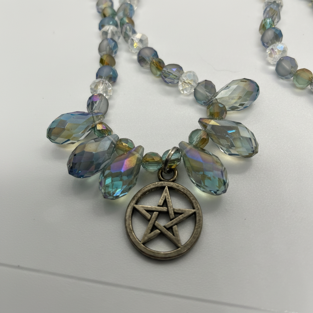 Close-up of iridescent crystal teardrop pendants and bronze pentagram charm on white background