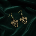 Pressed brass dragon earrings with green glass cathedral beads on dark velvet